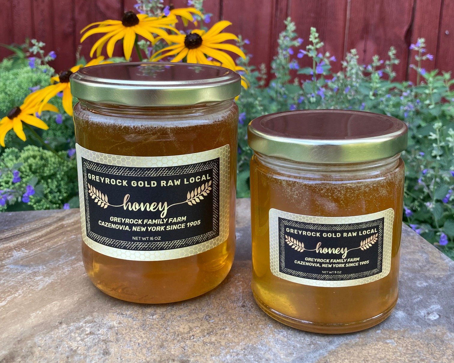 Two jars of honey surrounded by flowers at Greyrock Farm.